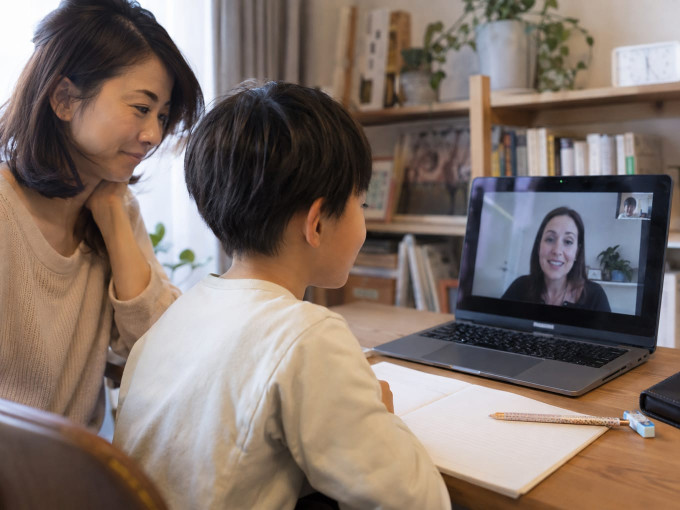 母親が見守る中ノートを開いて講師とオンライン英会話レッスンを受ける小学生の男の子